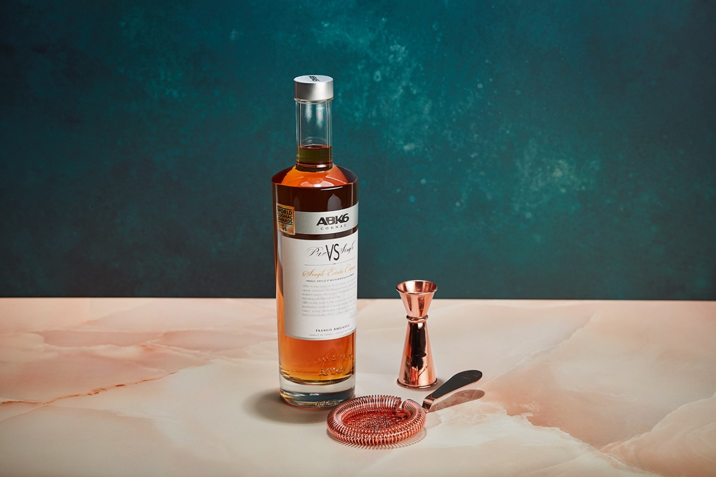 A bottle of alcohol next to a metal strainerDescription automatically generated